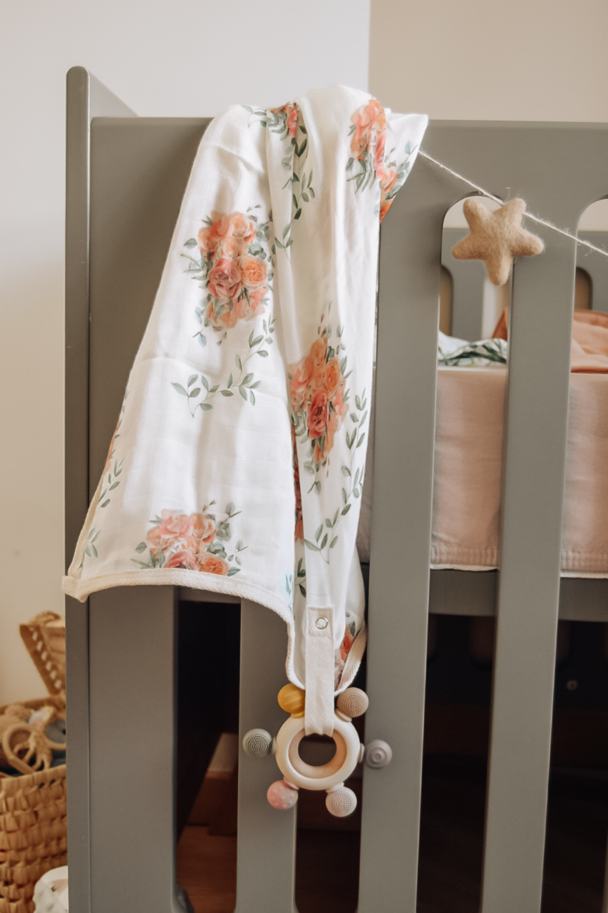 Rosen- Mulltuch am Babybett befestigt mit Spielzeug an der Schlaufe