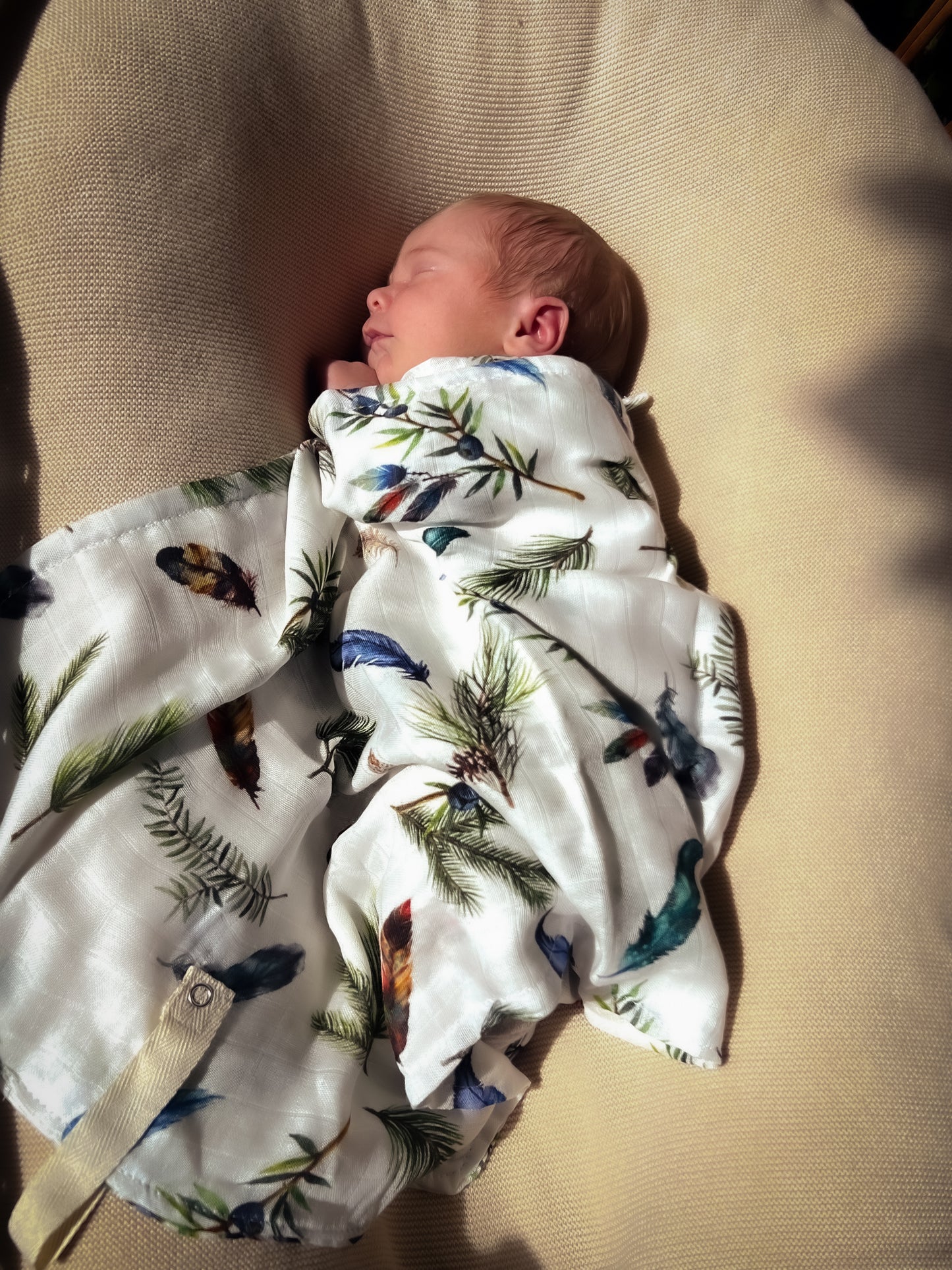 Schlafendes Neugeborenes liegt mit dem kleinen WandelWunder Tuch Federn als leichte Babydecke aus Bambusviskose und Baumwolle in der Sonne